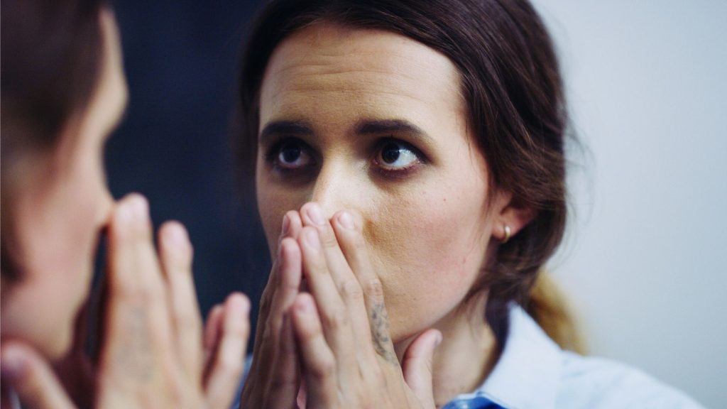 Person covering their mouth while looking in a mirror showing shame and secrecy